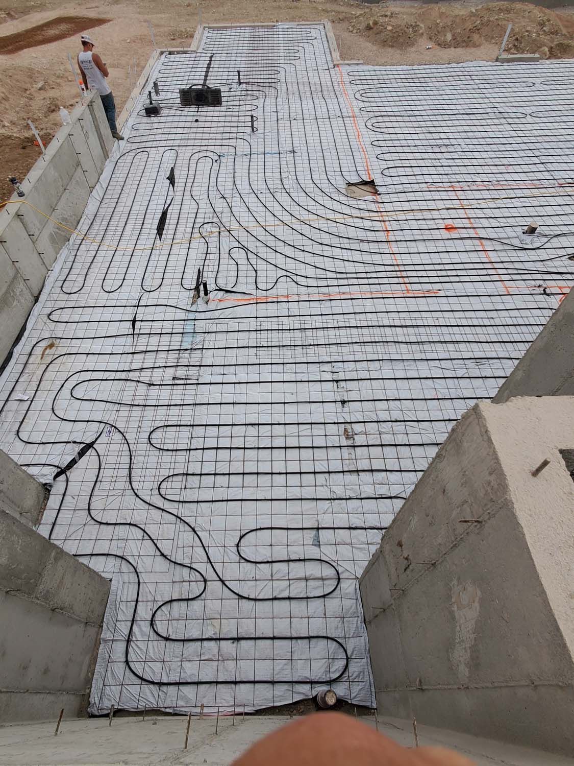 Radiant floor heating system installation with black tubing on a white reflective layer, outdoors at a construction site.