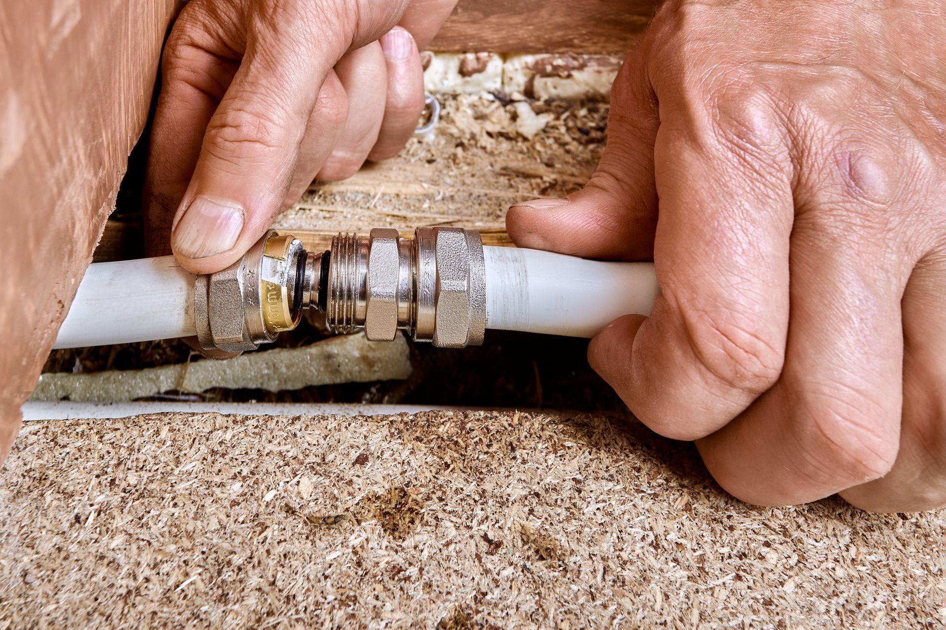 Hands connecting white pipe to metal fitting in a wooden space.