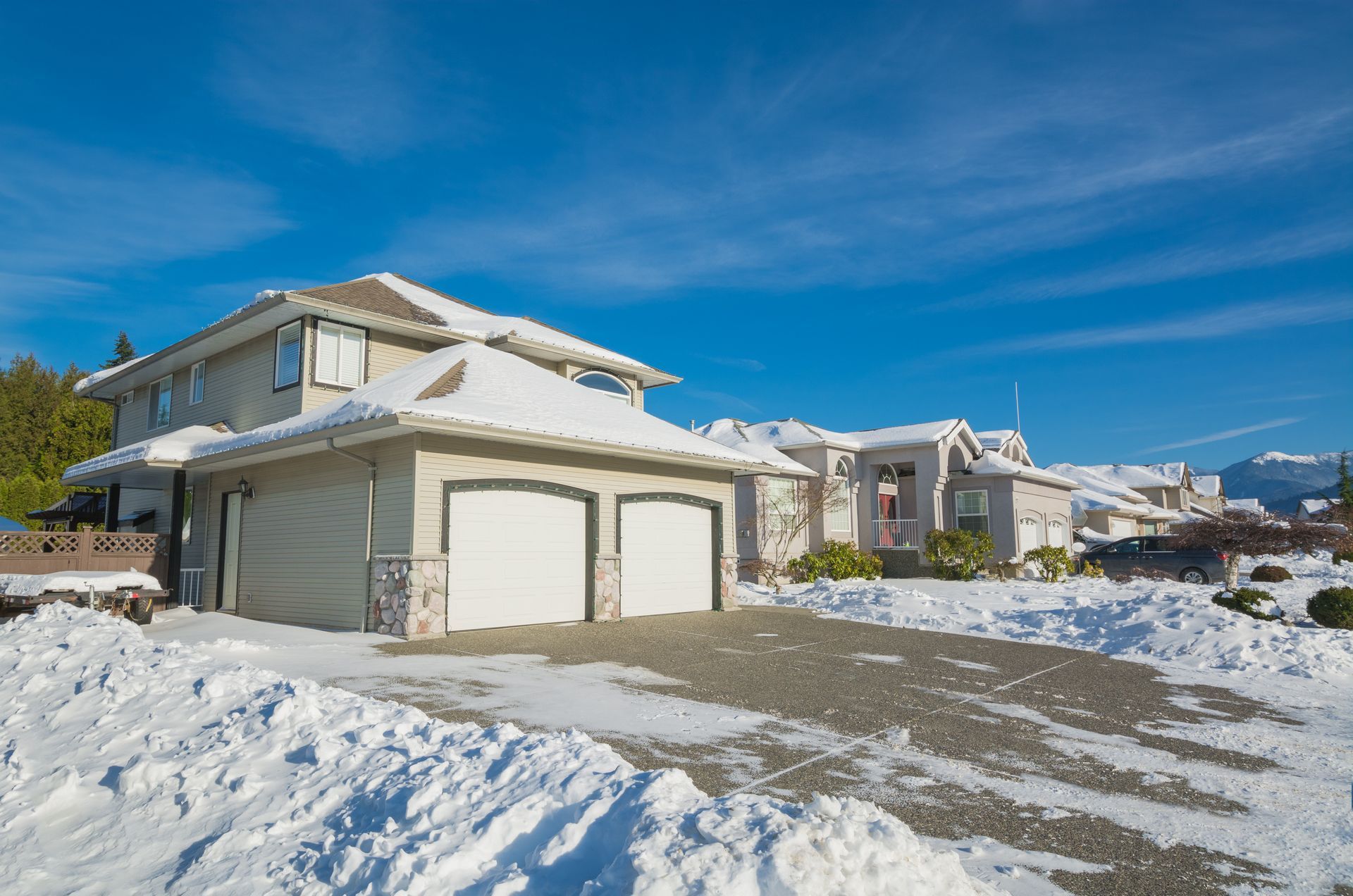Two-story house with a snow-covered roof and driveway, under a clear blue sky.