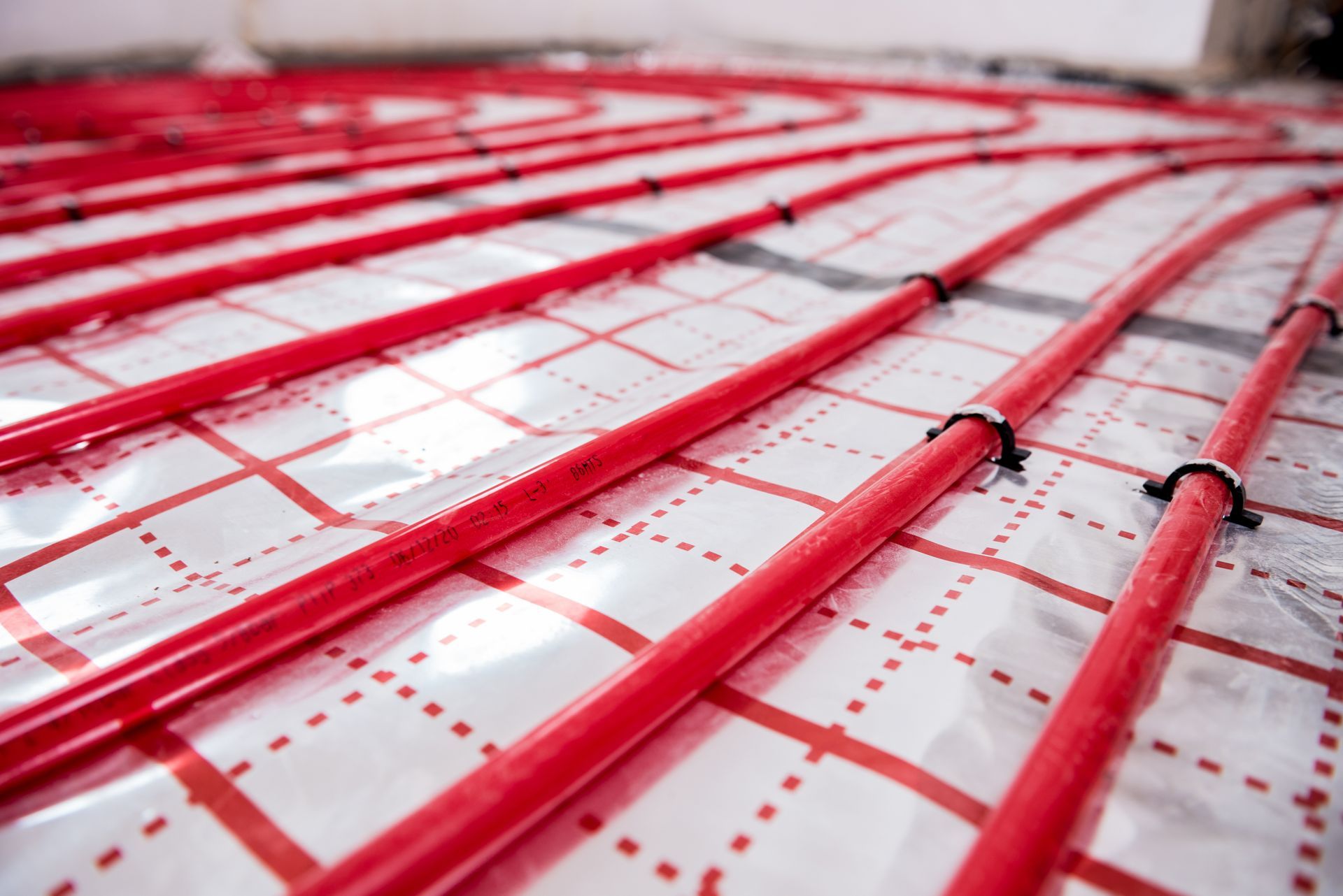 Red radiant floor heating pipes installed on a grid pattern over a reflective layer.