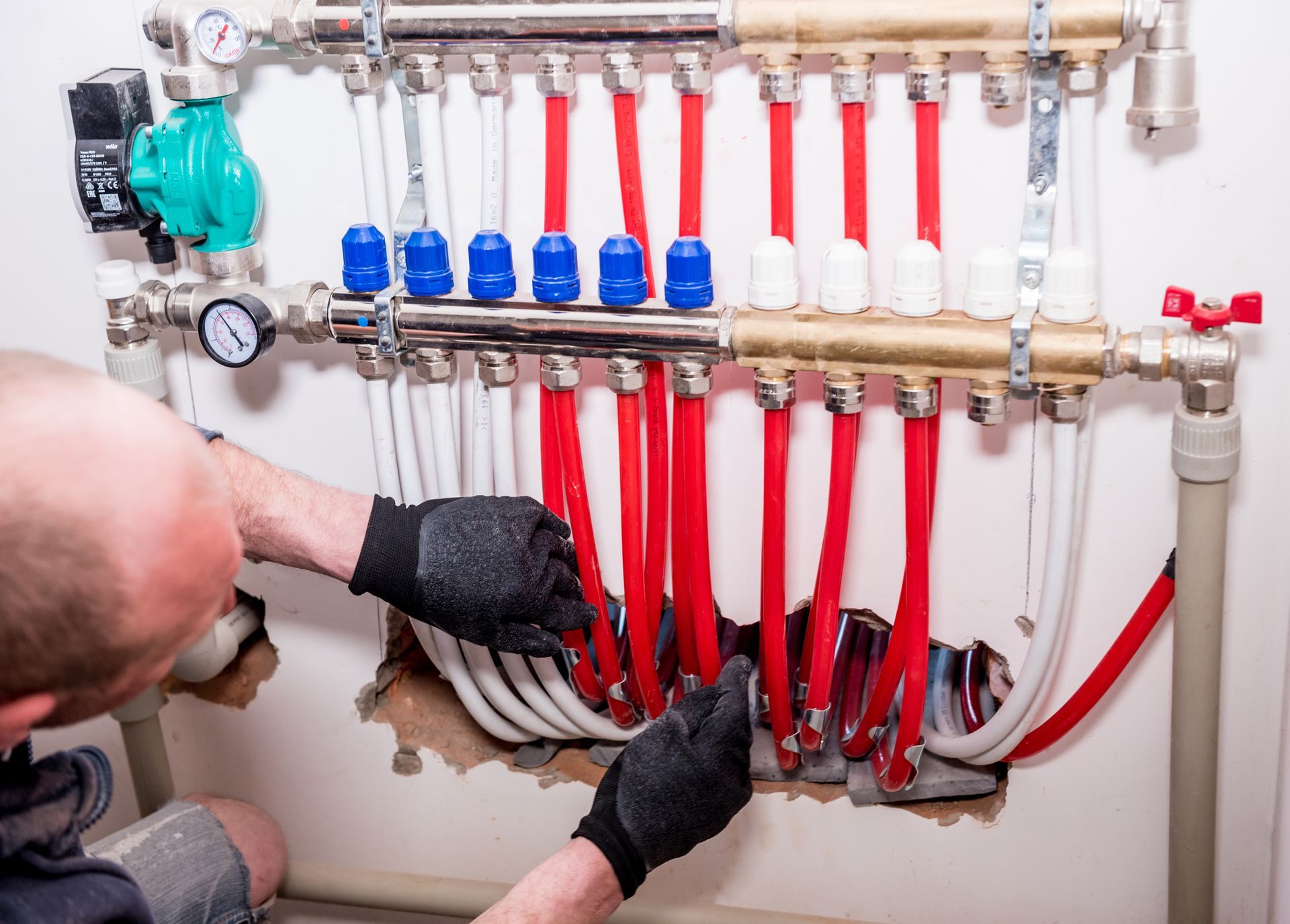 Person working on a radiant floor heating manifold system with red and white pipes.