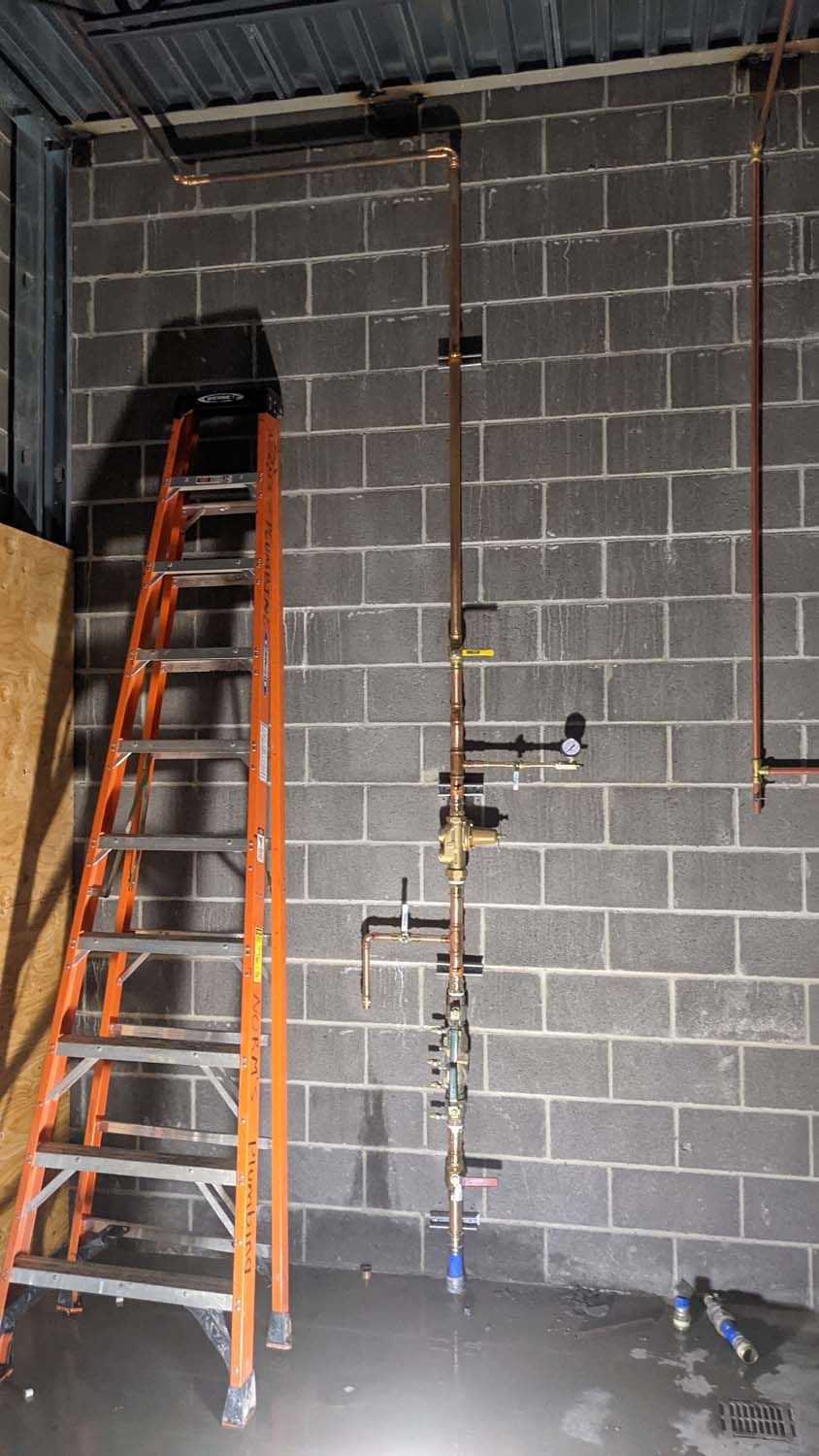Orange ladder next to copper pipes against a cinder block wall, plumbing installation in progress.
