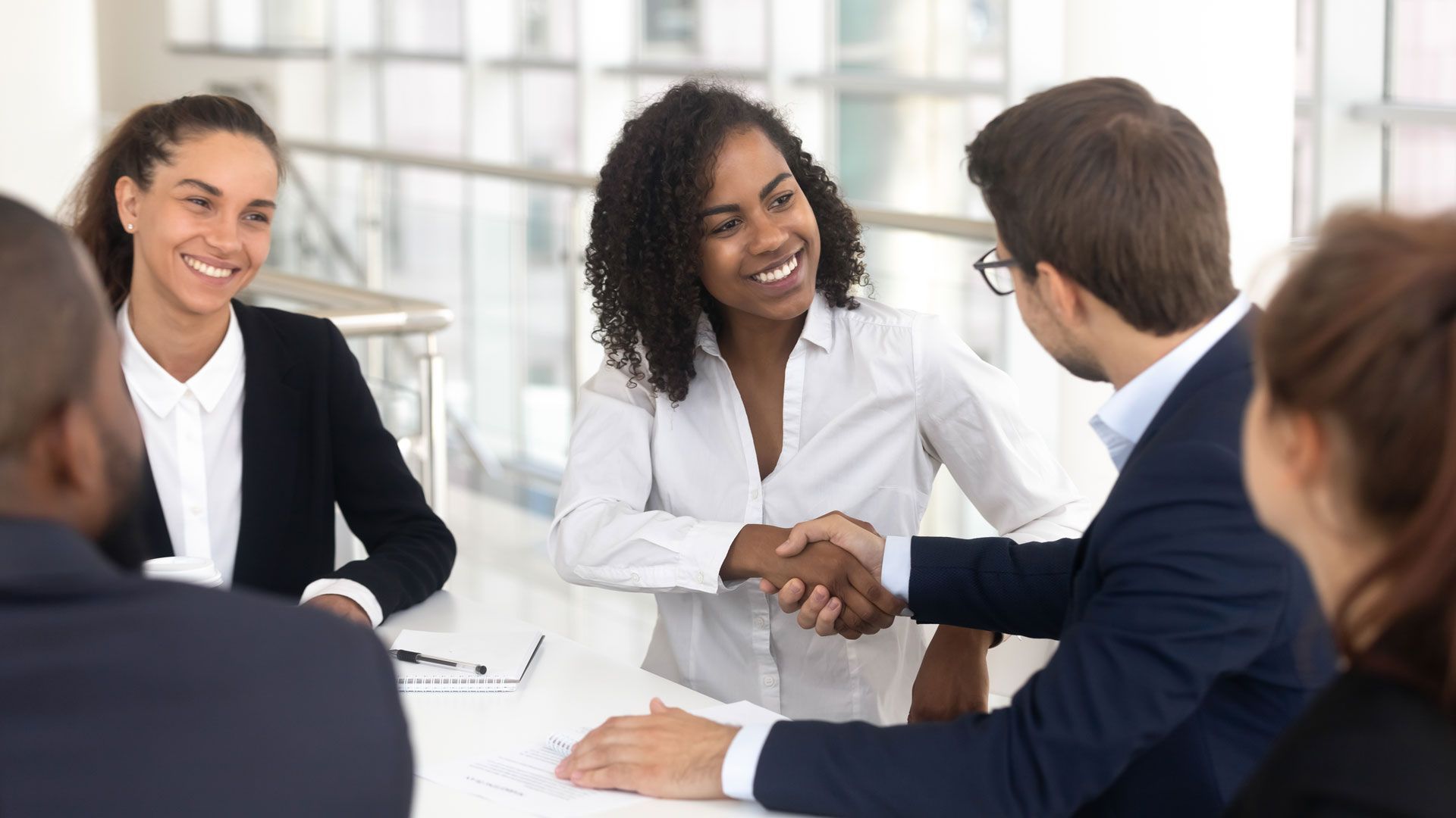 A group of people are sitting around a table shaking hands.