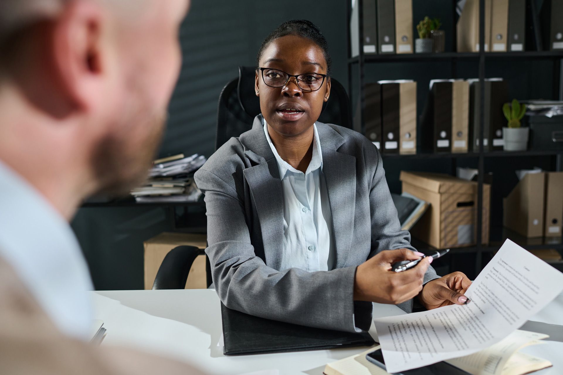 A woman is sitting at a desk talking to a man.
