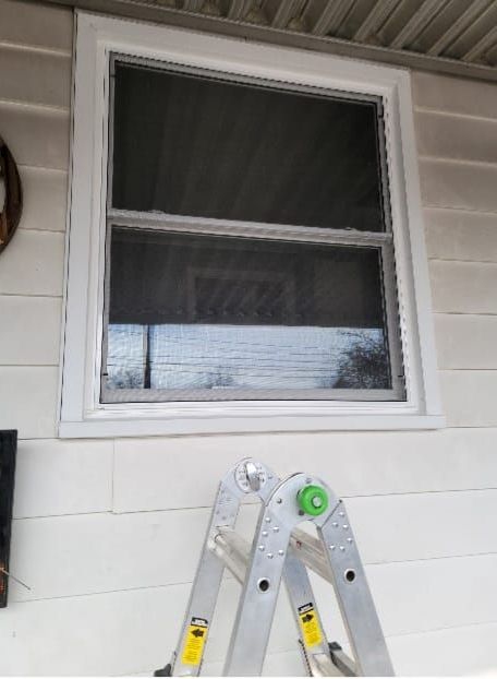 A ladder is sitting in front of a window on a white house.