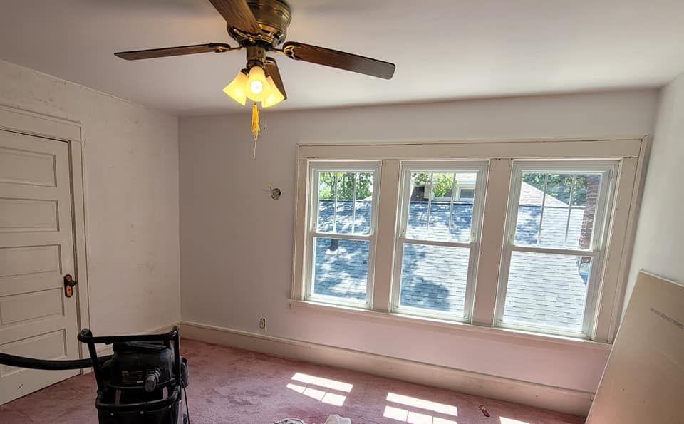 An empty room with a ceiling fan and three windows