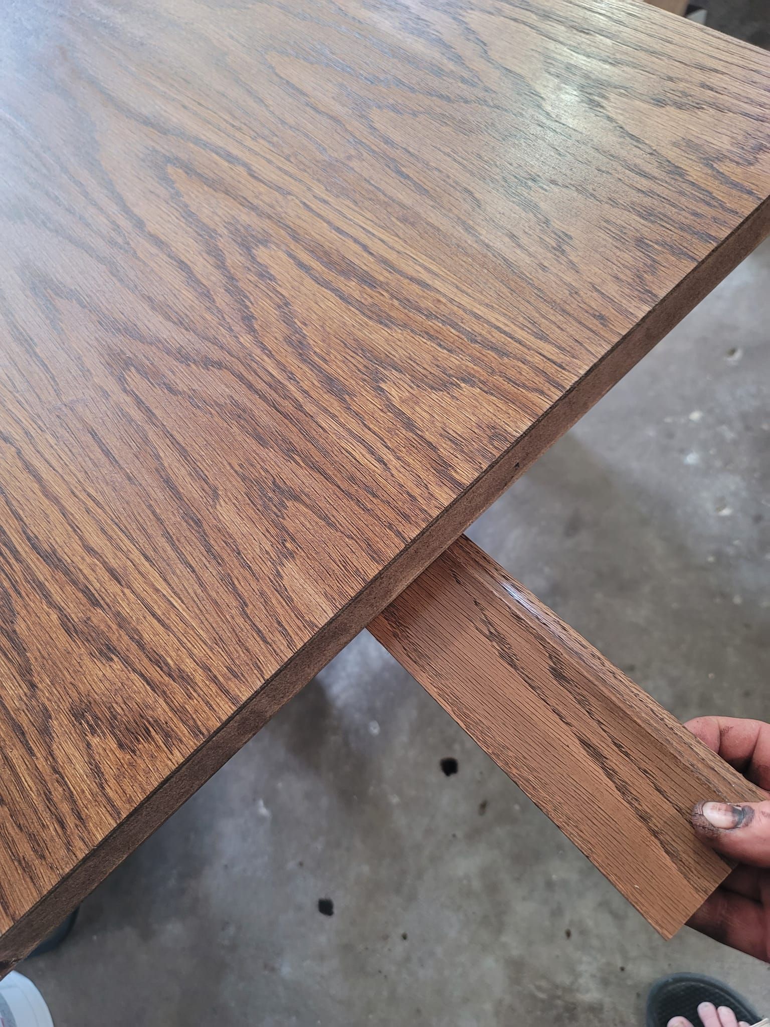 A person is holding a piece of wood on top of a wooden table.
