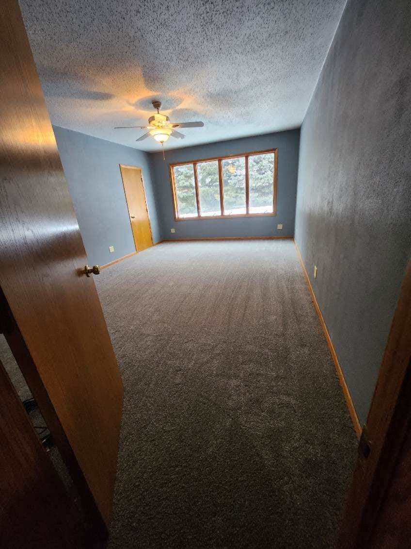 An empty living room with a ceiling fan and a lot of windows.