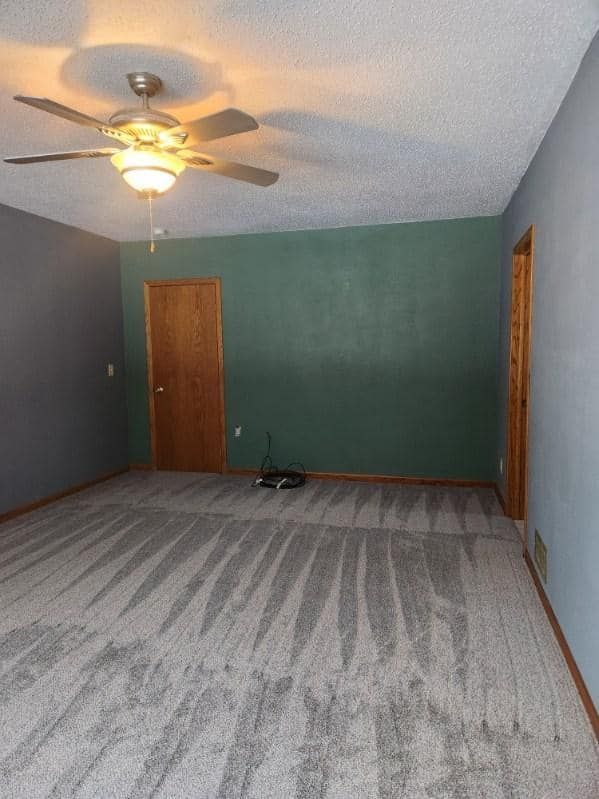 An empty living room with a ceiling fan and a door.