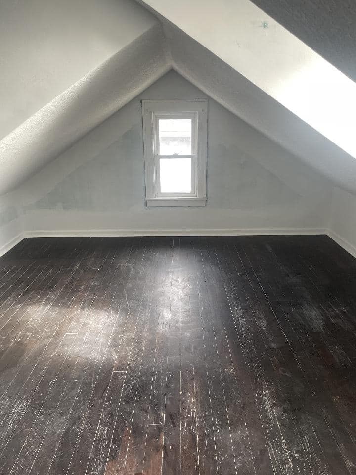 An empty attic with a window and a wooden floor.