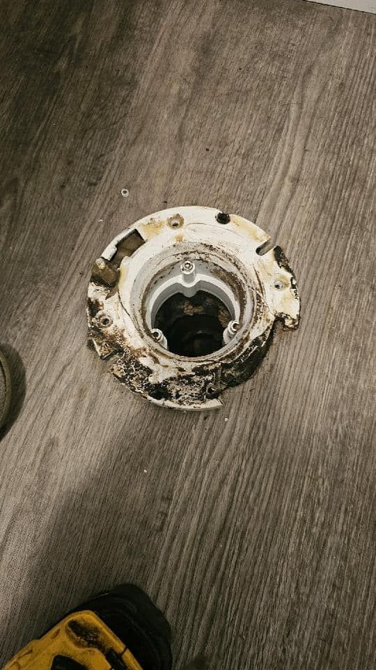 A close up of a toilet flange on a wooden floor.