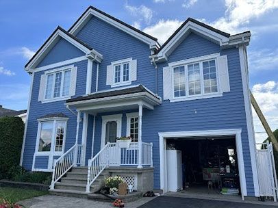Une grande maison bleue avec des garnitures et des volets blancs et un garage. Travaux de peinture extérieure soignée