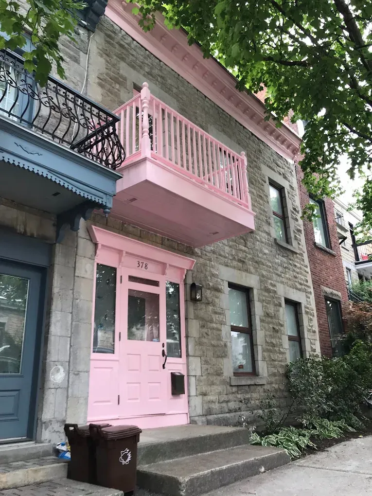 Peinture extérieure d’une maison rose avec balcon et rampes visibles à l’avant.
