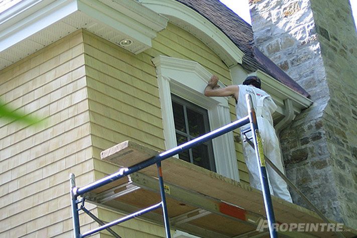 Application de peinture sur corniche de chalet en cèdre avec échafaudage sécurisé