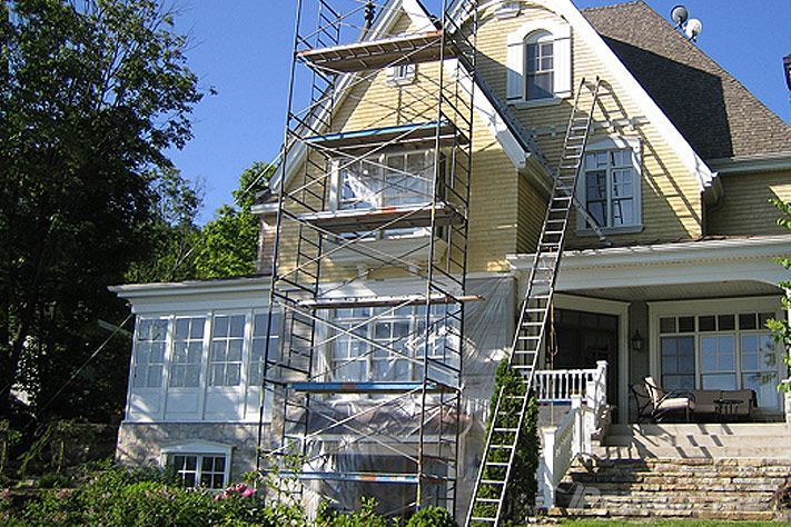 Maison jaune à étages avec échafaudage pour peinture extérieure