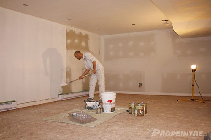 Peintre appliquant une première couche de peinture au rouleau dans un sous-sol rénové