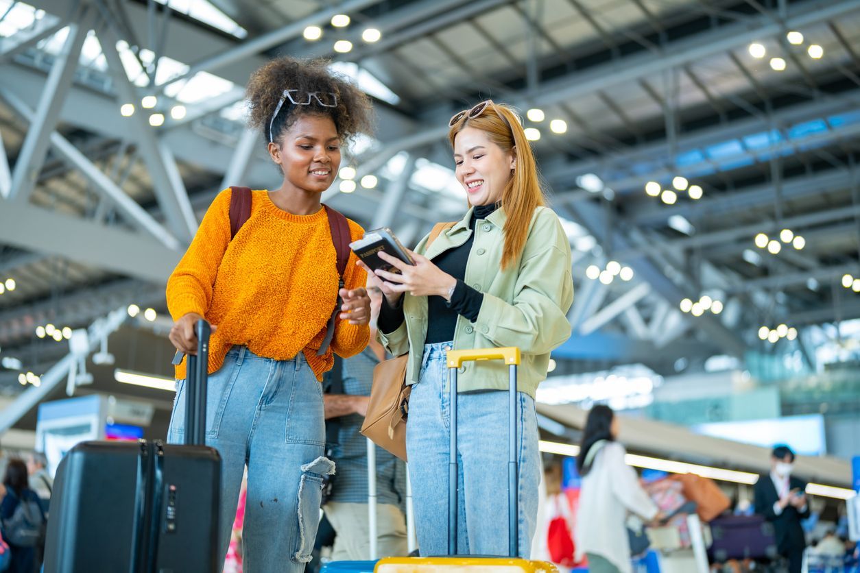 Two travelers with luggage consult a passport or mobile device in a bright, modern airport terminal.