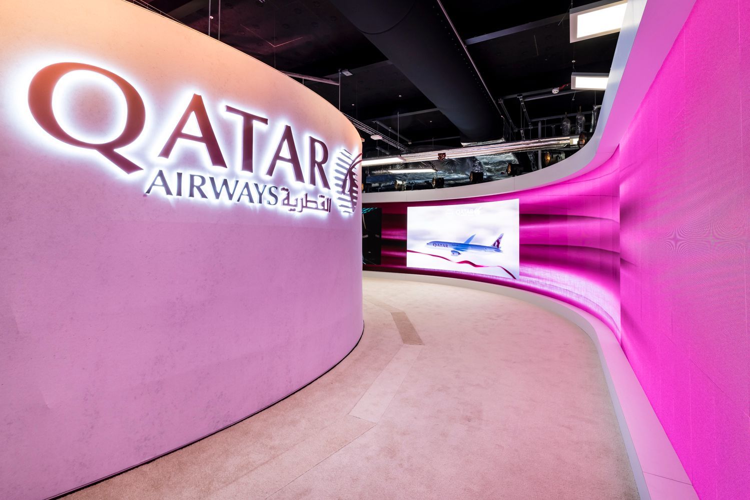 A sign for qatar airways is lit up on a pink wall