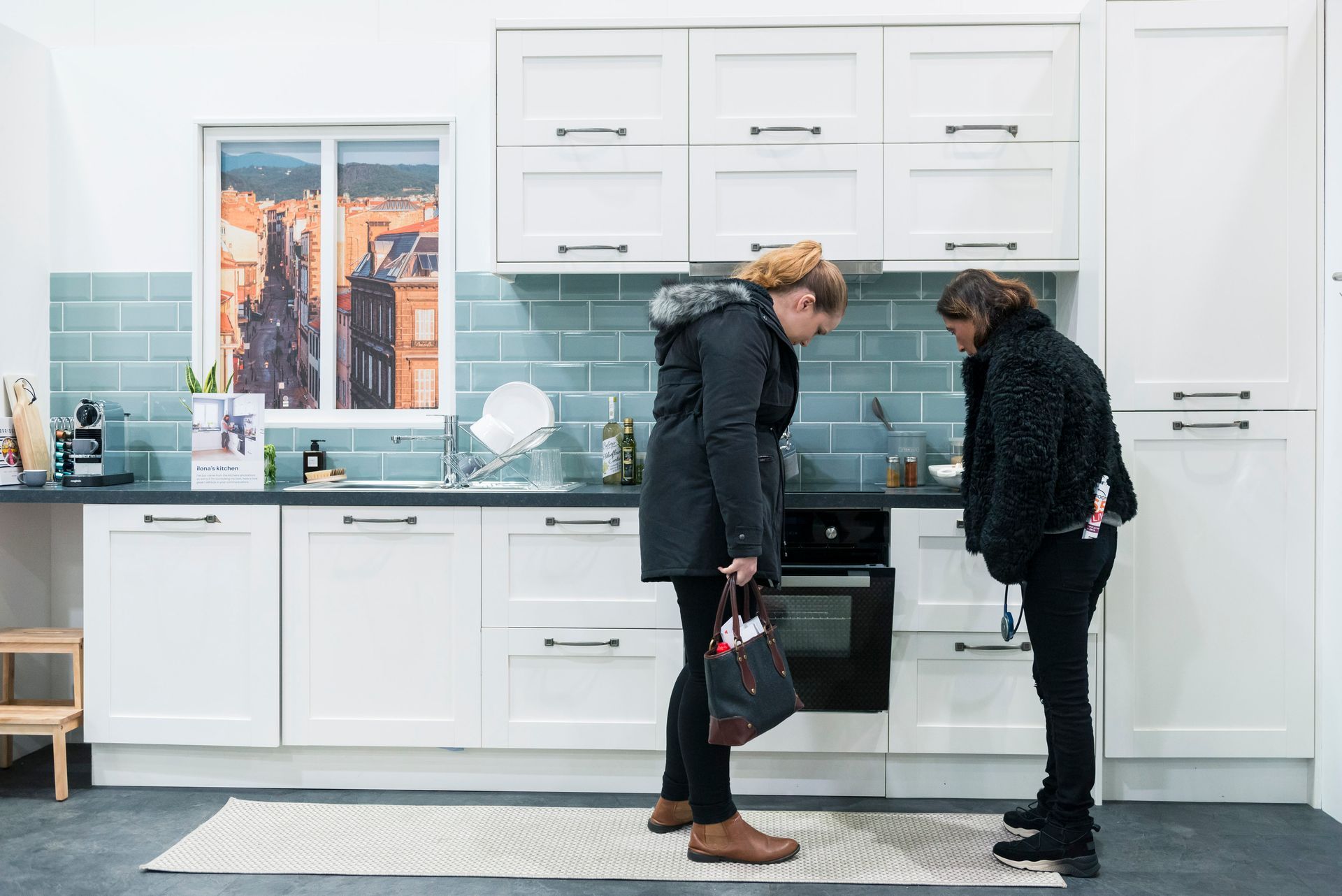 Two women are standing in a kitchen looking at a stove.