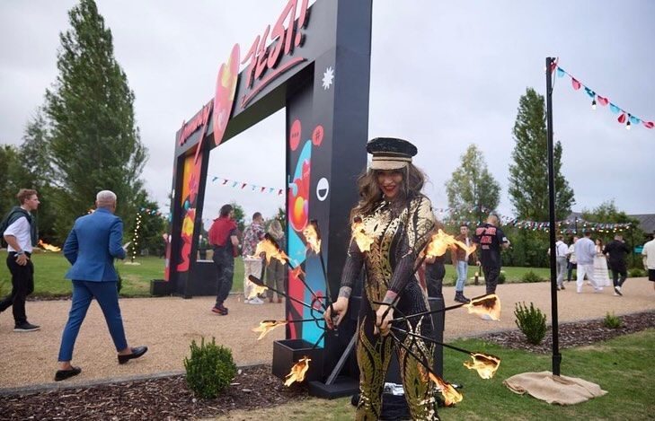A woman in a gold costume is standing in front of a large sign.