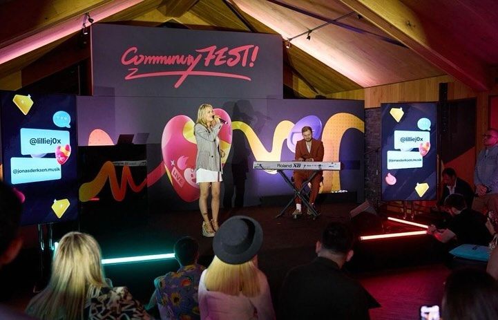 A woman is singing into a microphone in front of a crowd at a community fest.