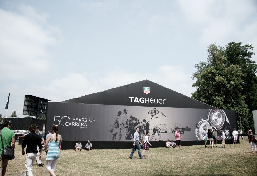 People are walking in front of a large sign that says tagheuer