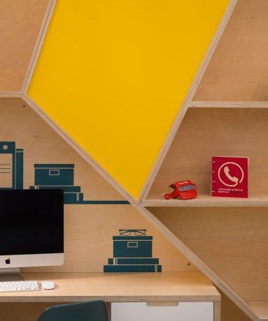 A computer sits on a desk in front of a yellow wall