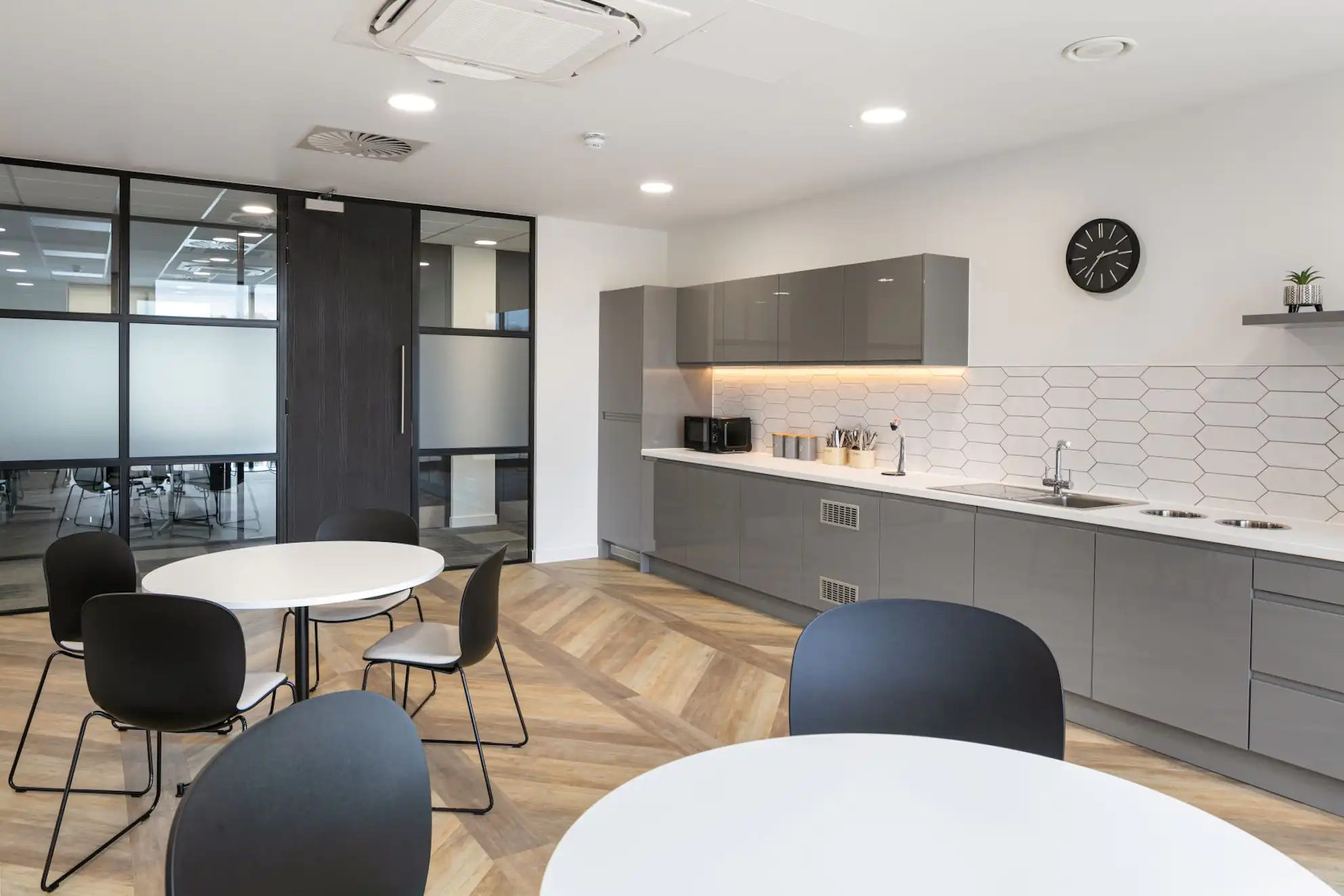 A kitchen with tables and chairs and a clock on the wall.