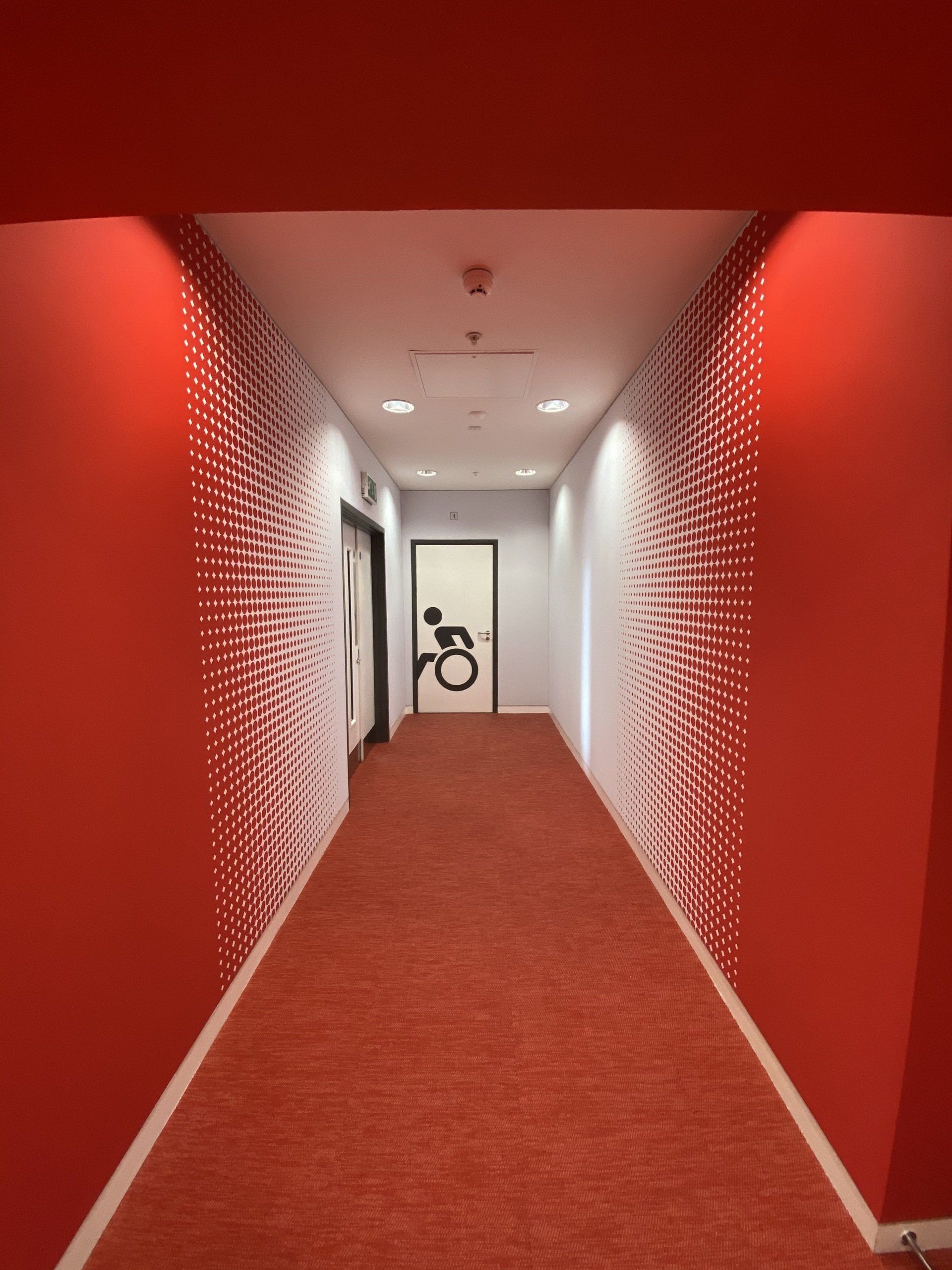 A hallway with red walls and a door with a wheelchair on it