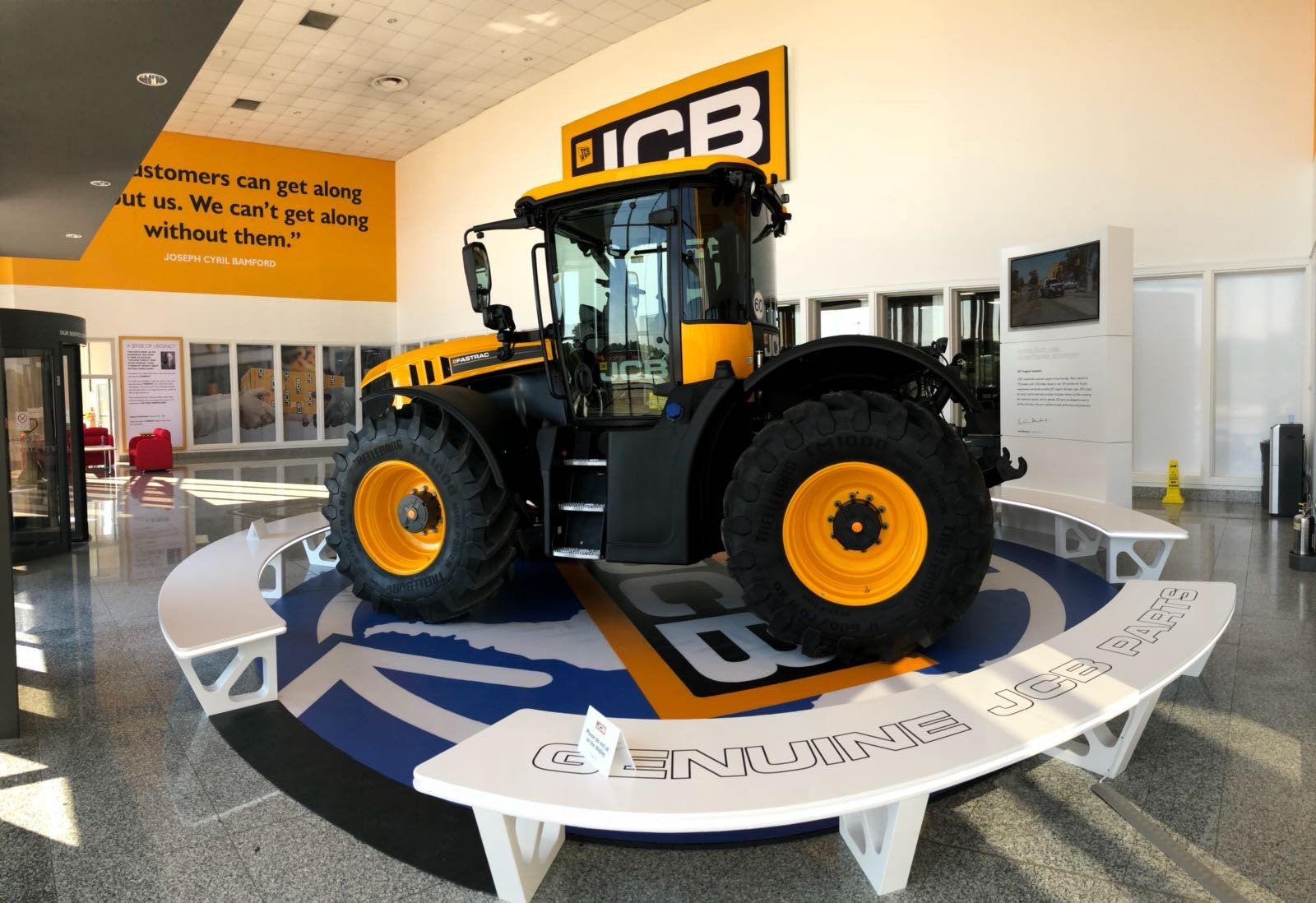 A yellow and black tractor is on display in a building with a jcb logo on the wall.
