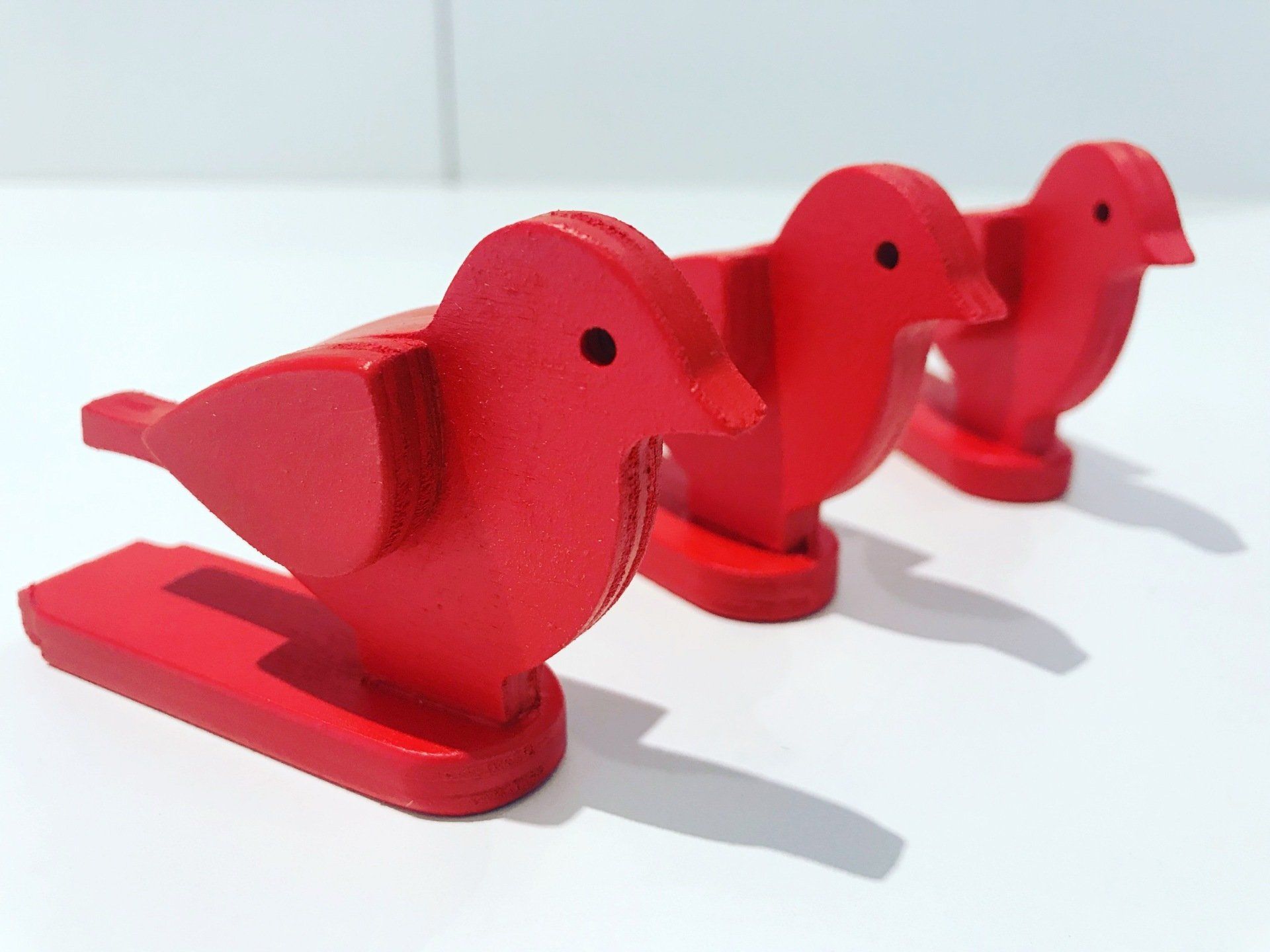 Three red birds are lined up on a white surface