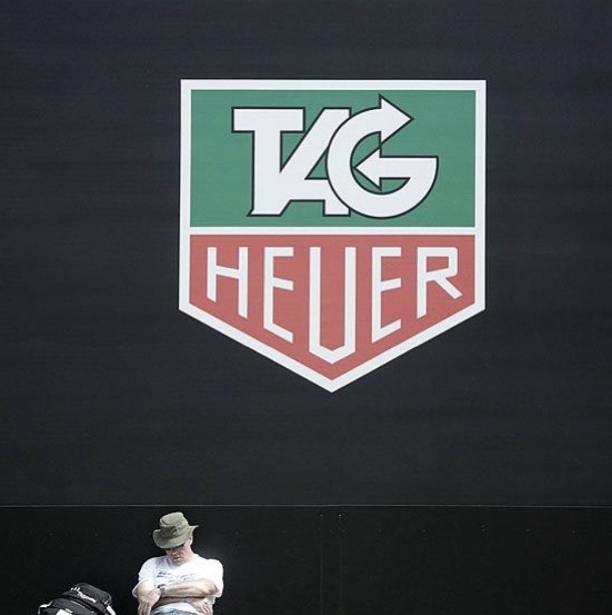 A man sits in front of a large tag heuer logo
