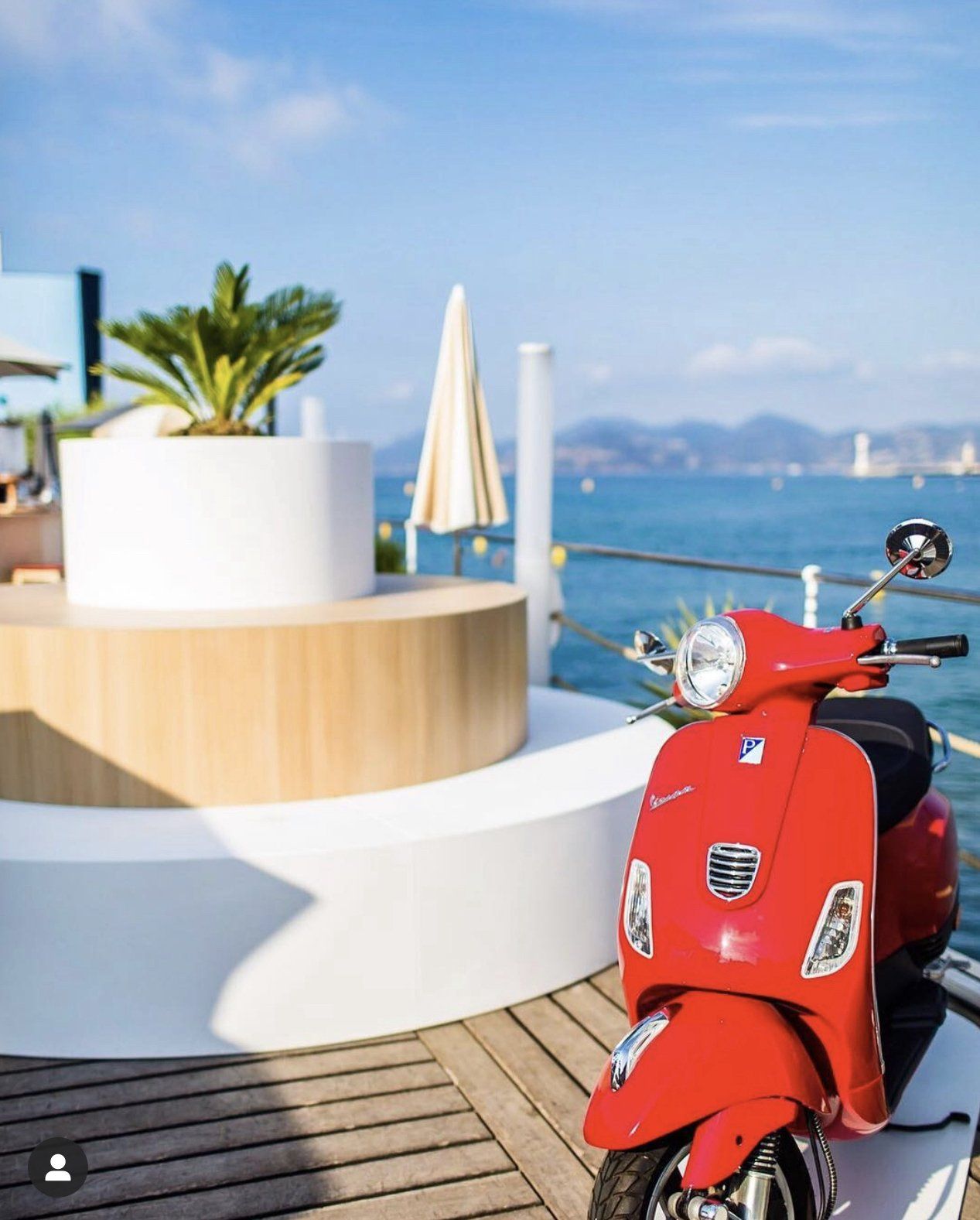A red scooter is parked on a wooden deck overlooking the ocean