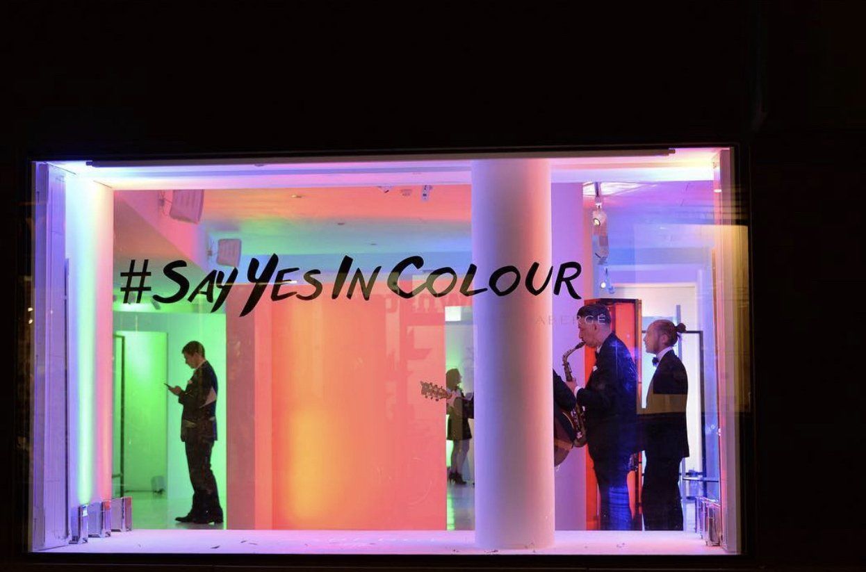 A group of people are standing in front of a window that says say yes in colour.