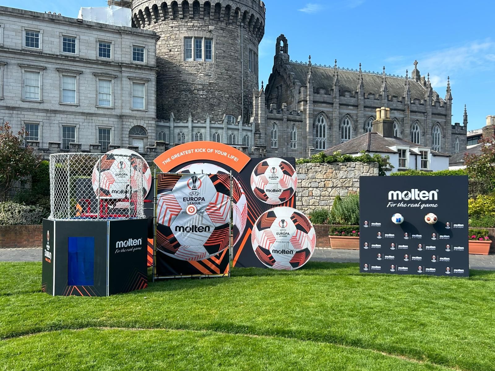 A group of soccer balls are sitting on top of a lush green field in front of a castle.