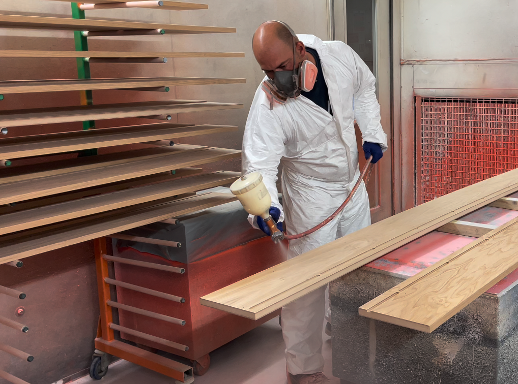 A man wearing a mask is spray painting a piece of wood.