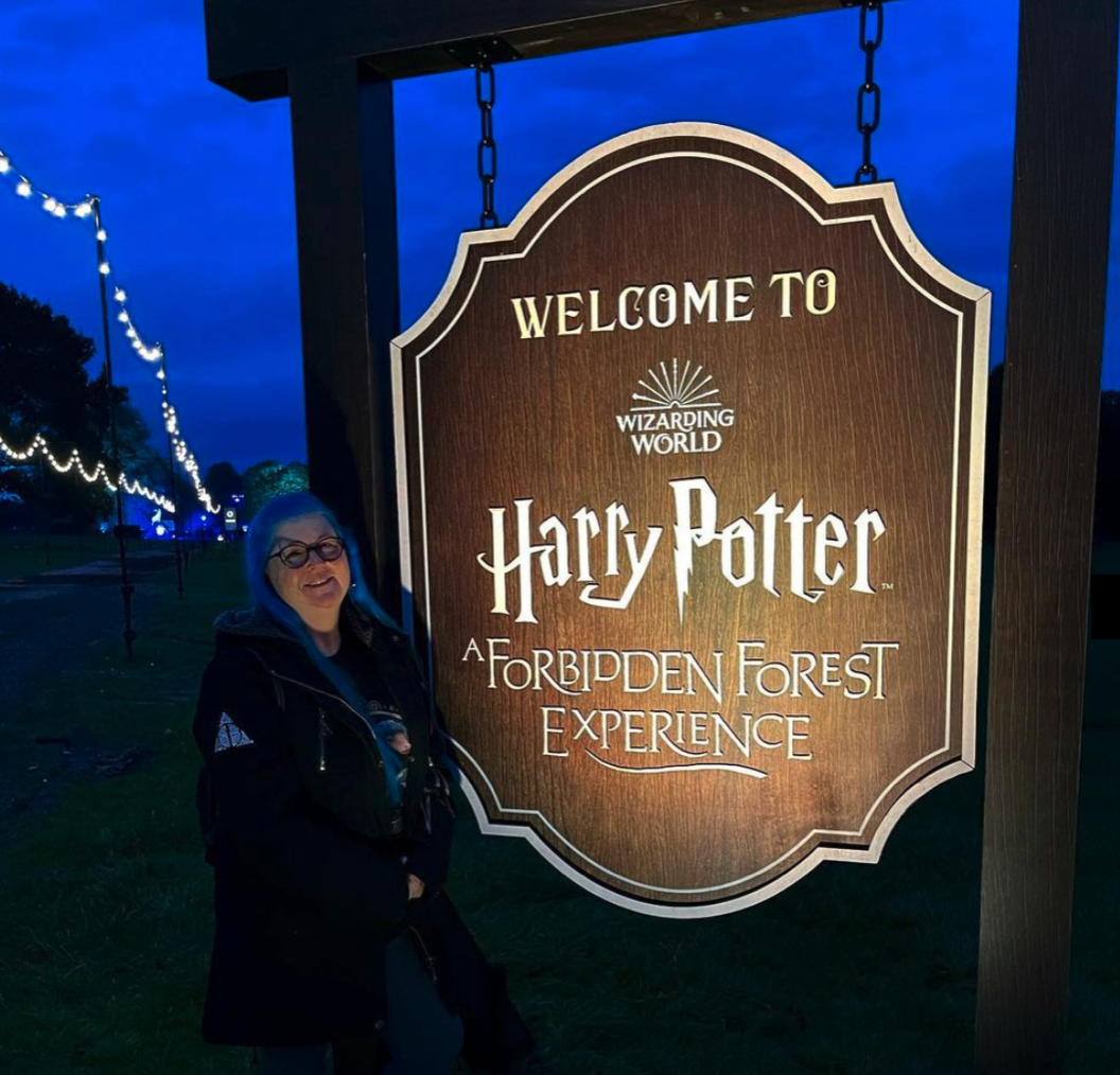 A woman stands in front of a welcome to harry potter sign
