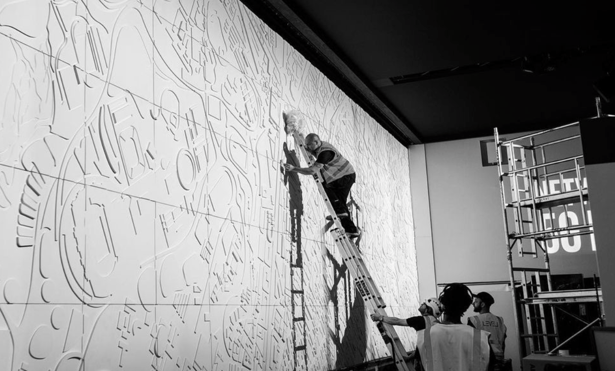 A black and white photo of a man on a ladder painting on a wall.