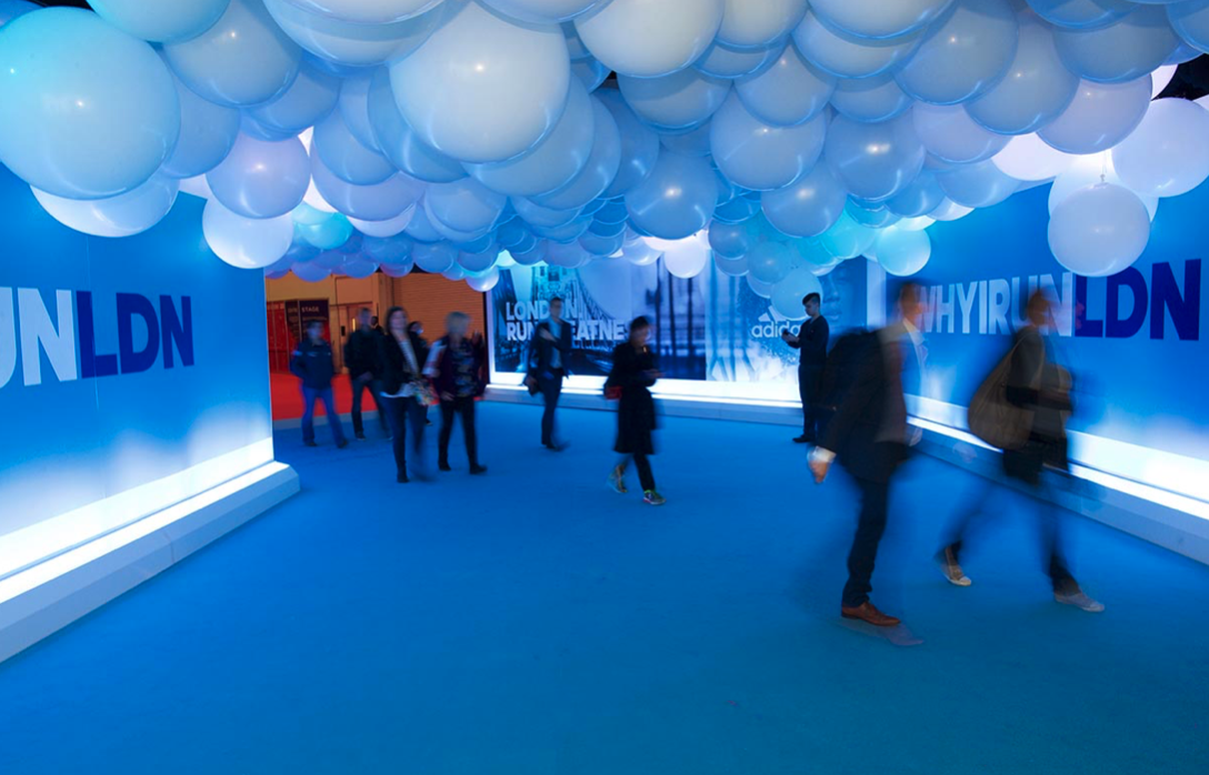 A group of people are walking down a hallway with balloons hanging from the ceiling.