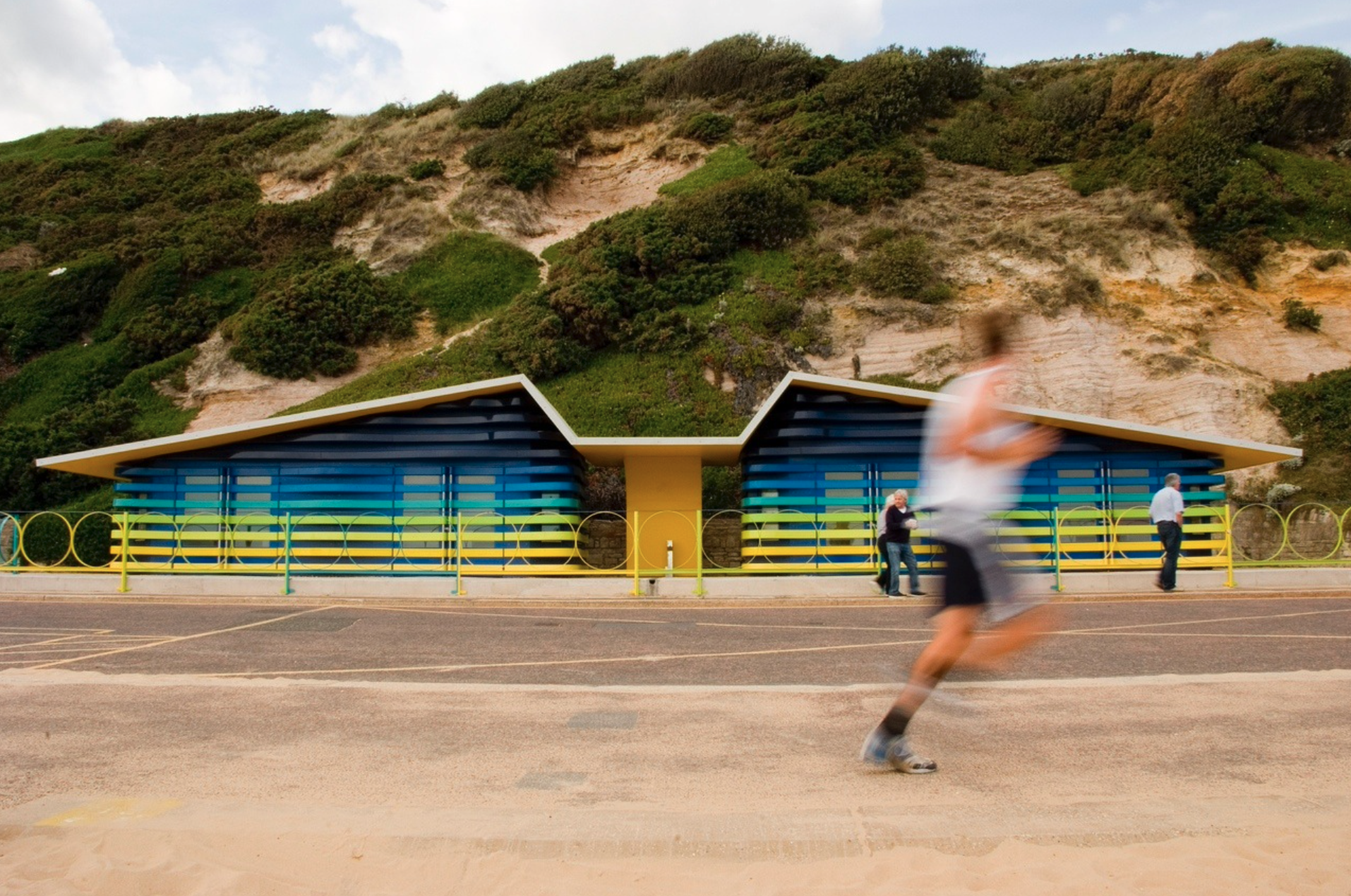 A man is running in front of a blue and yellow building