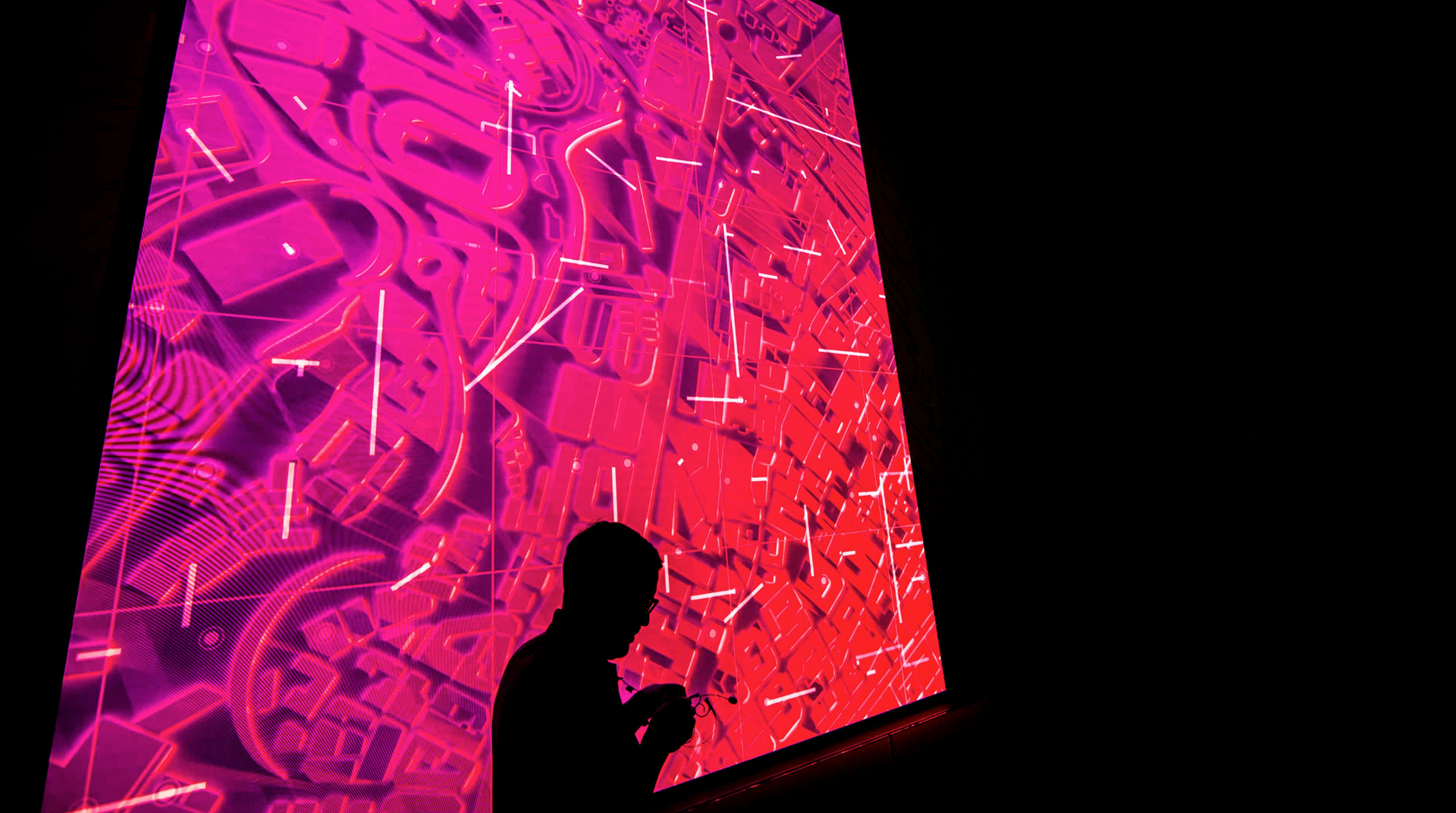 A man is standing in front of a large screen looking at his phone.
