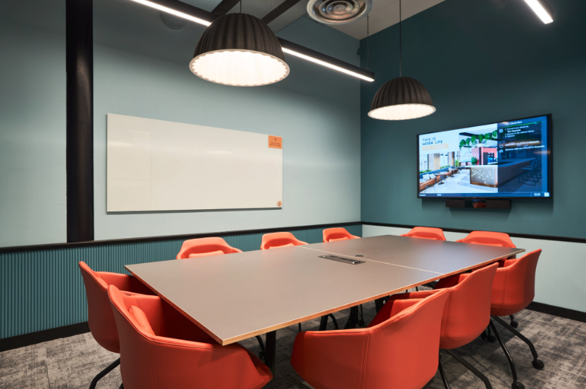 A conference room with a long table and orange chairs.