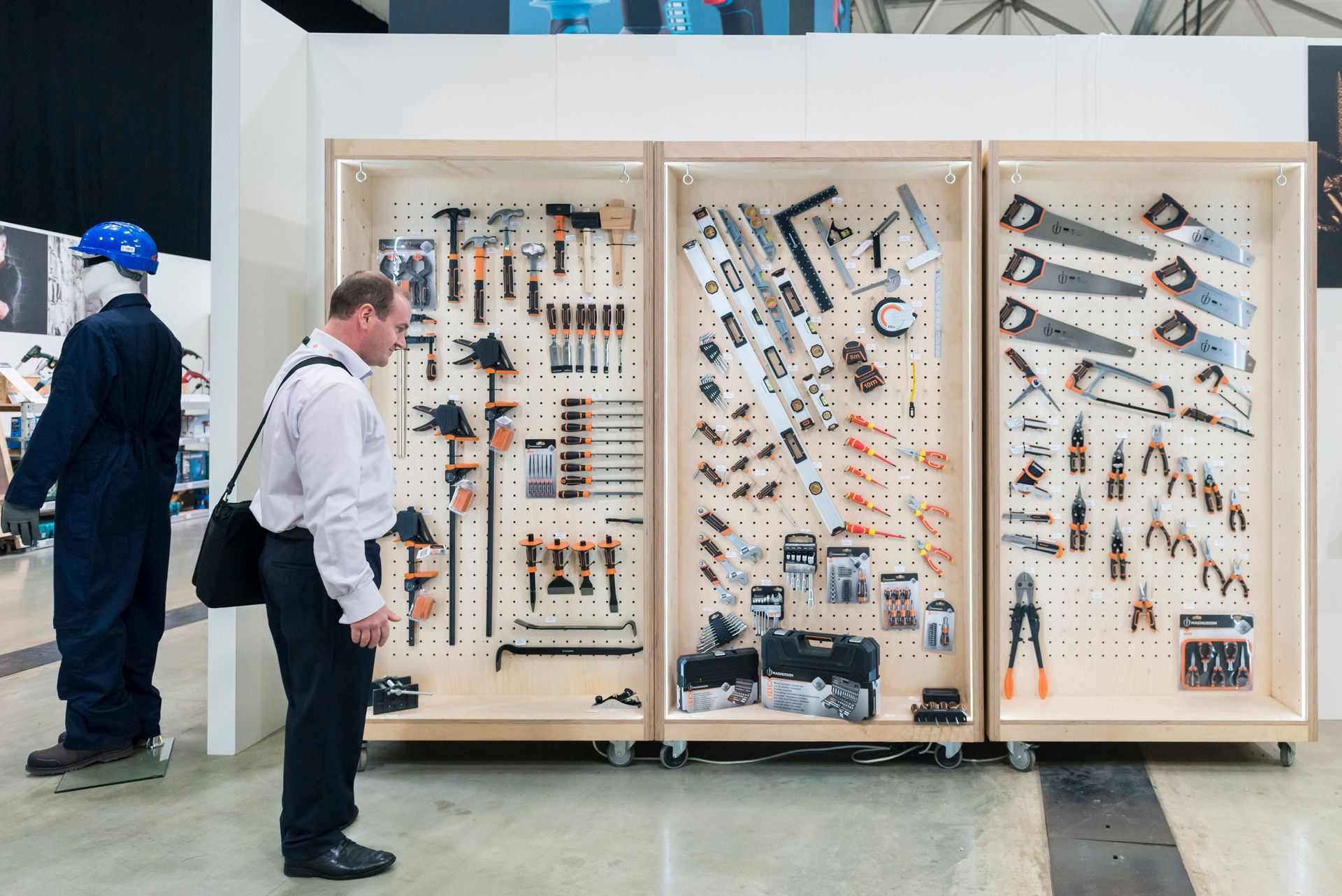 Two men are standing in front of a wall filled with tools.
