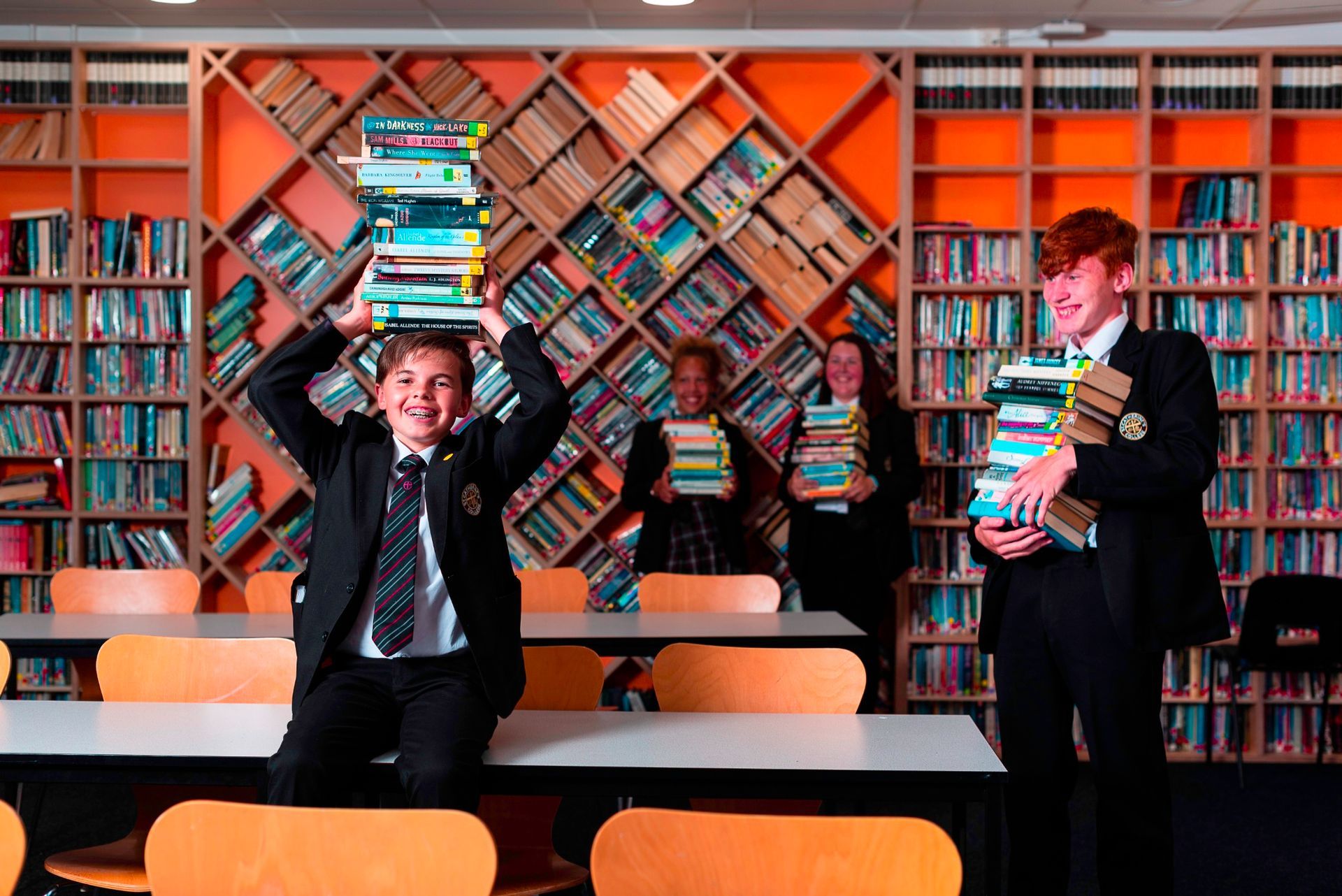 A boy is holding a stack of books over his head in a library.