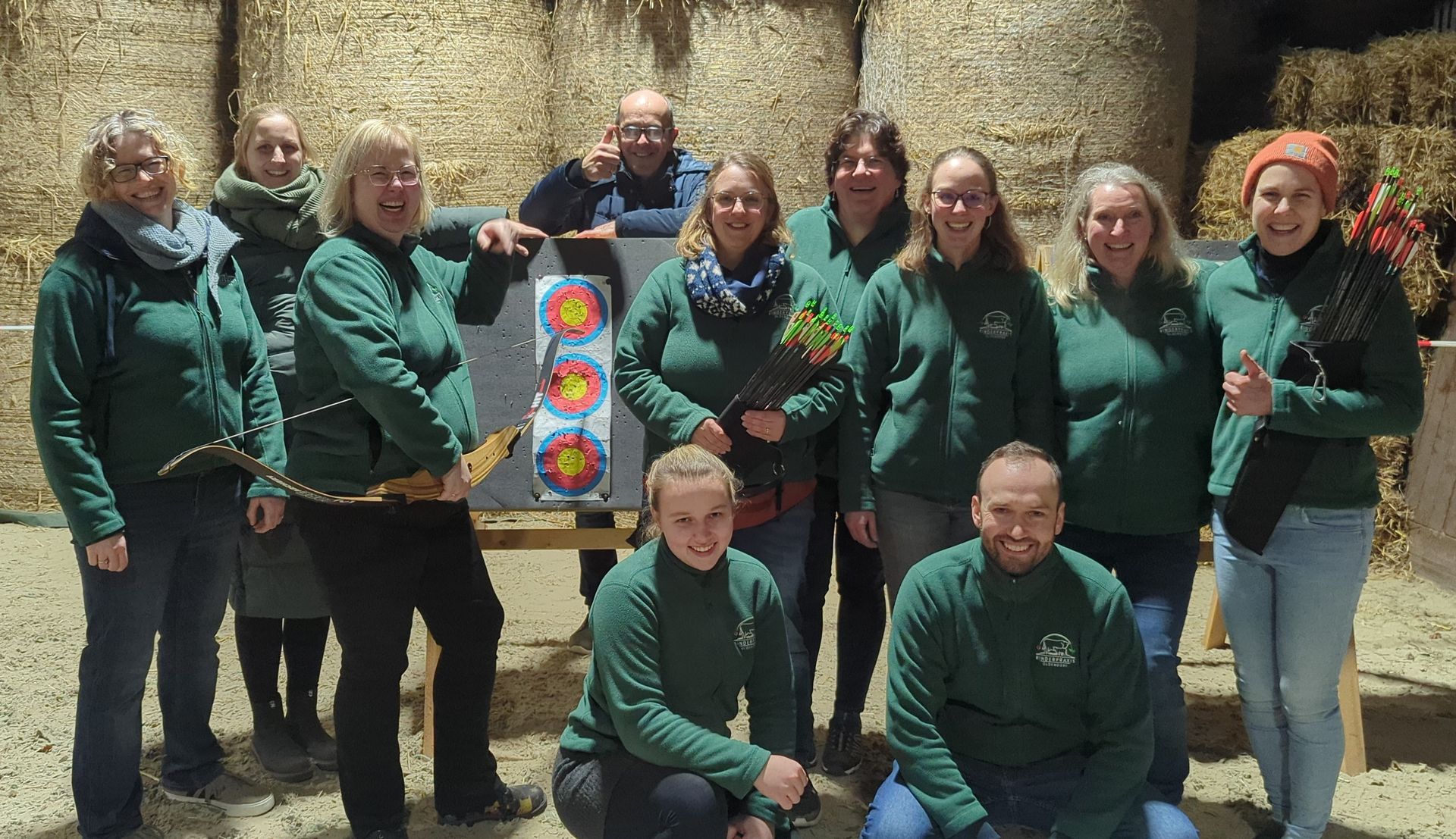 Eine Gruppe von Personen in grünen Hemden posiert mit einer Zielscheibe vor Heuballen.