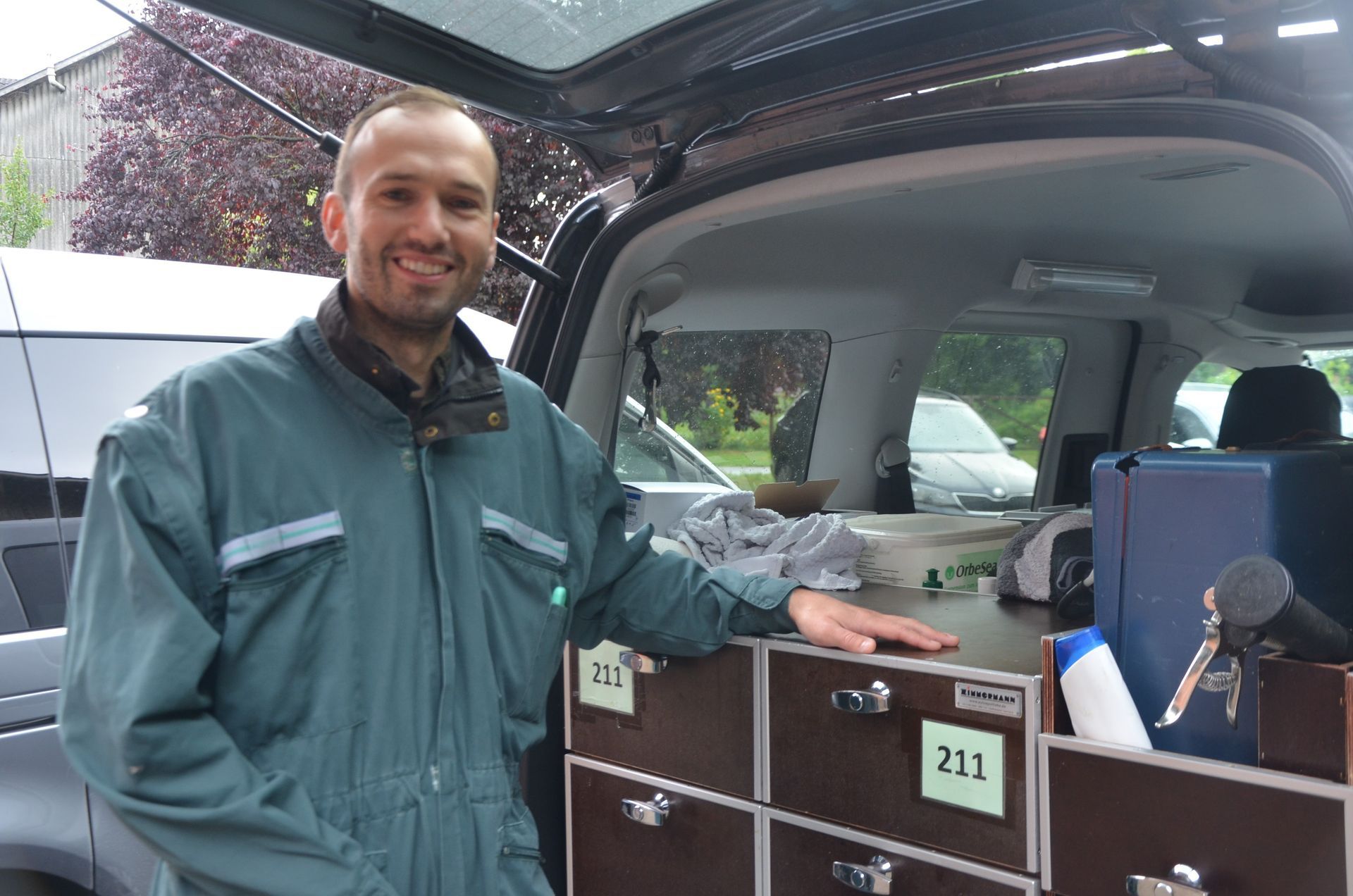 Tierarzt in einem grünen Overall lächelt neben einem Lieferwagen mit Schubladen im Freien.