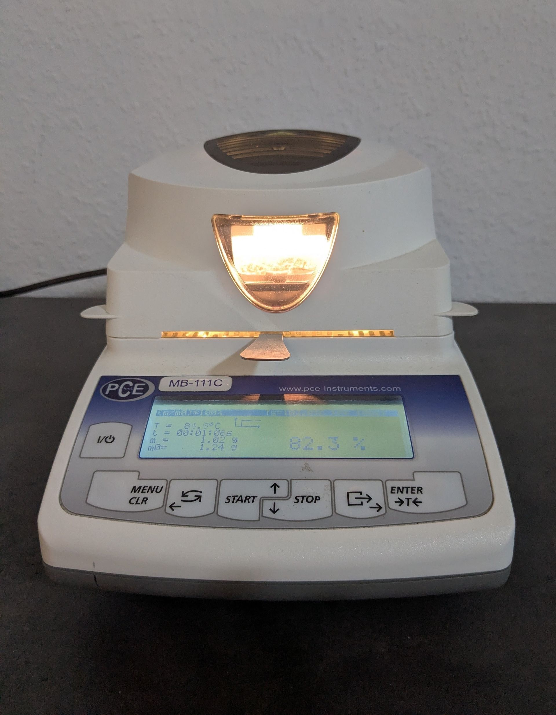 Weißer und blauer Feuchtigkeitsanalysator; das Display zeigt „Ende“ und ein Ergebnis an. Die Ofenbeleuchtung ist eingeschaltet.