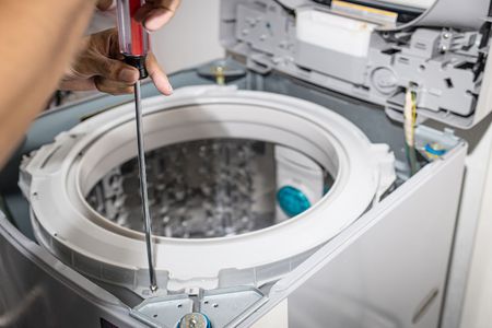 A person is fixing a washing machine with a screwdriver.