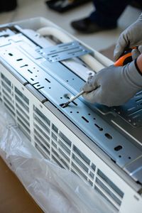 A person is fixing an air conditioner with a screwdriver.