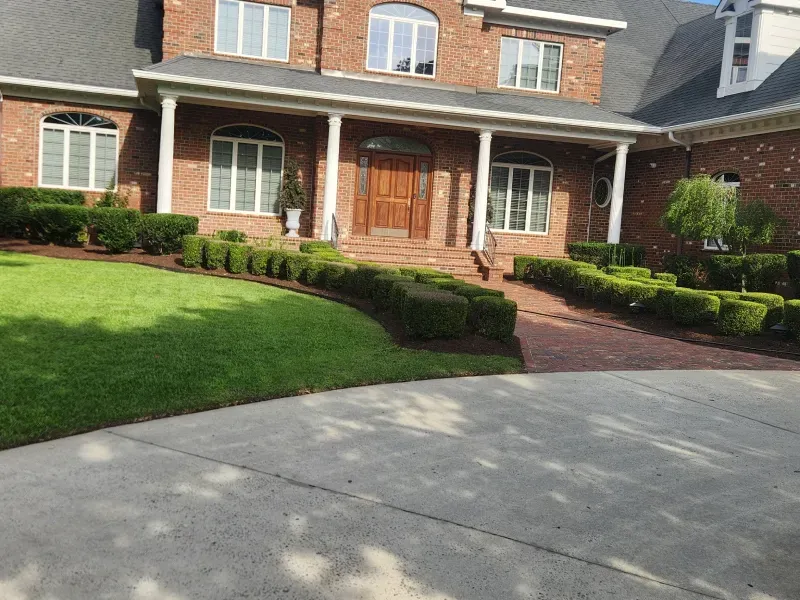 Brick house with manicured lawn and walkway. Box hedges line a brick path leading to the front door.
